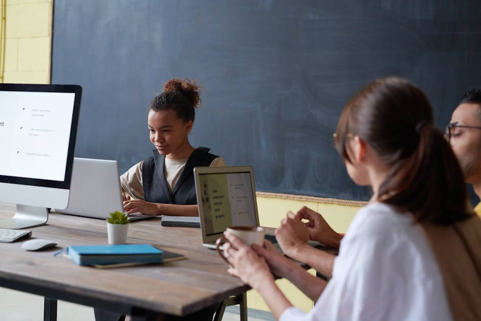 Group of young adults engaged in digital learning with laptops and desktops in a contemporary classroom